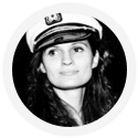A black and white photo of a person with long hair wearing a maritime captain's hat.